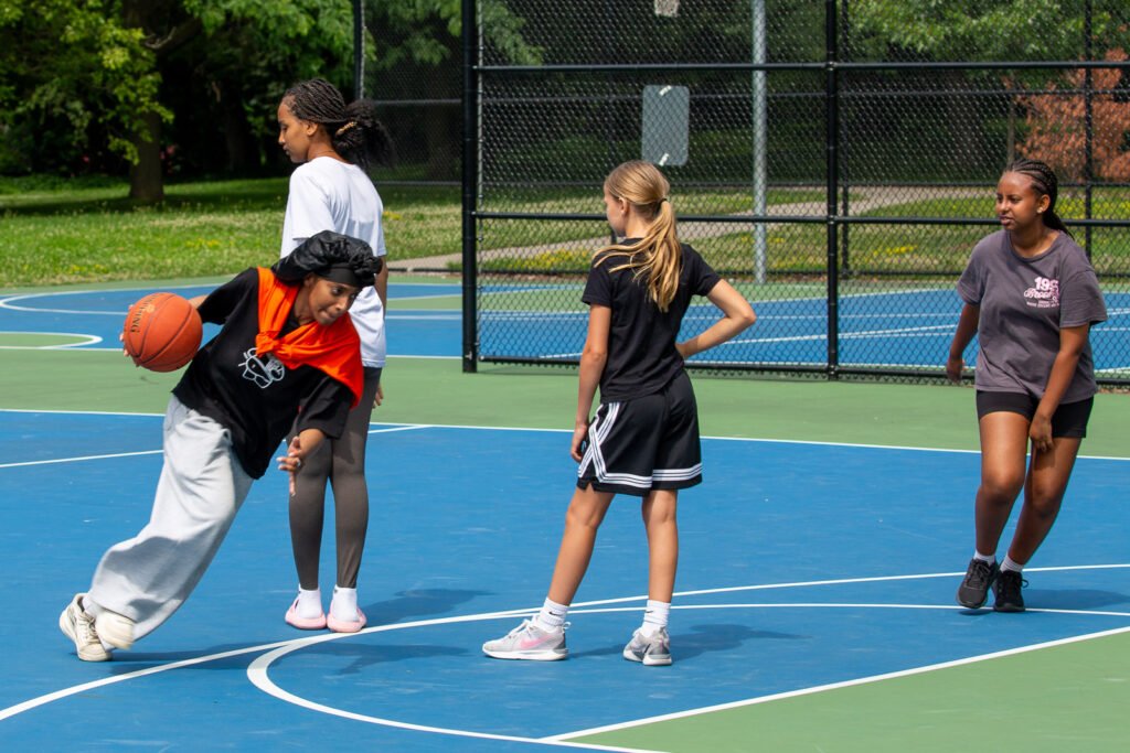 Players practising basketball together on an outdoor court during the summer program